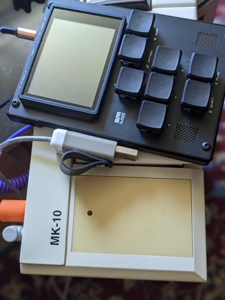 An M8 sitting on top of a Commodore MK-10. A purple cable goes from the keyboard to the M8 MIDI in port. A USB power adapter is seen plugged into the keyboard.