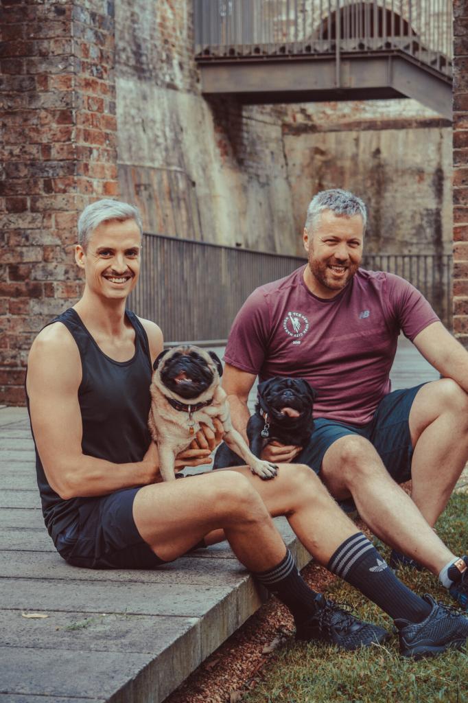 Two men in athletic gear holding their pugs
