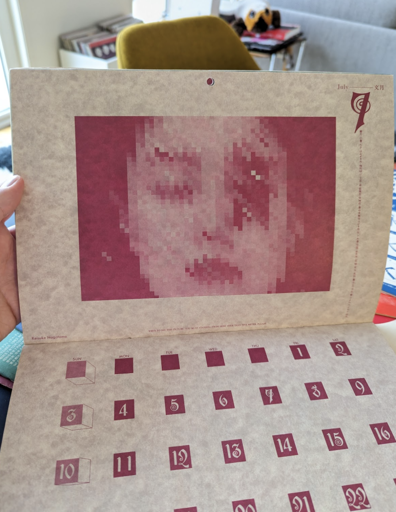 July month has a pixelated picture of a woman face. Art by Keisuke Nagatomo. Under the illustration a warning is noted : "When to see this picture, you must standing from here over than five meter please"