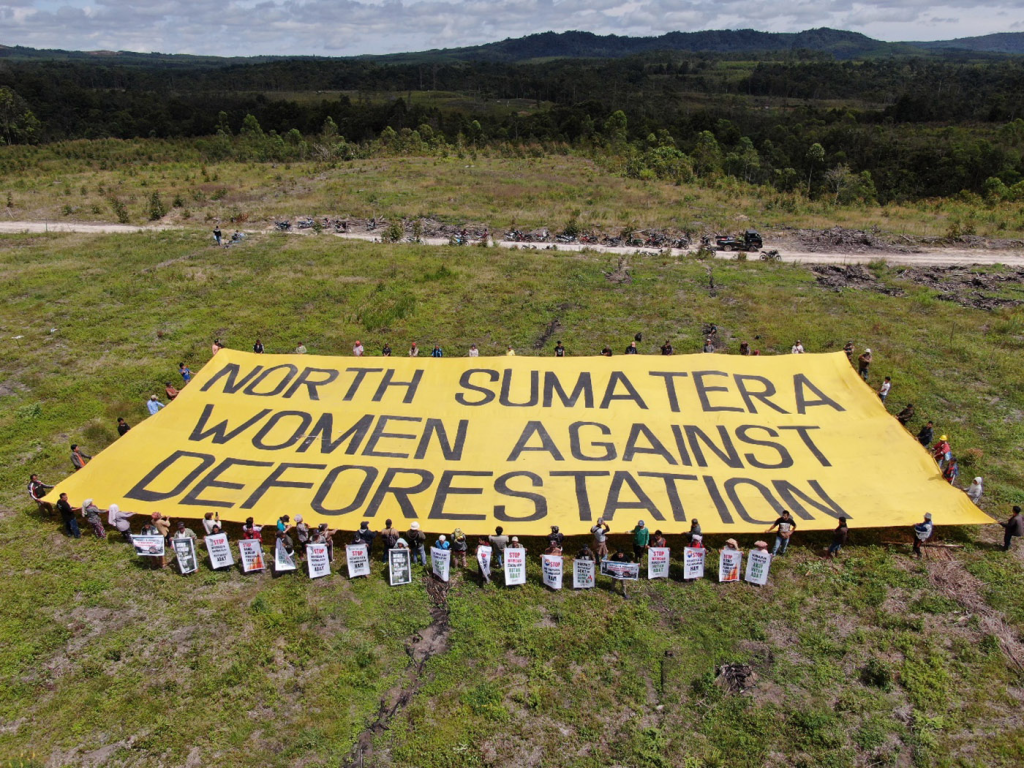 Indigenous Batak communities in North Sumatra hold a giant banner in protest of unresolved land conflicts and deforestation on Indigenous lands by PT. Toba Pulp Lestari. Photo by KSPPM, October 2022.