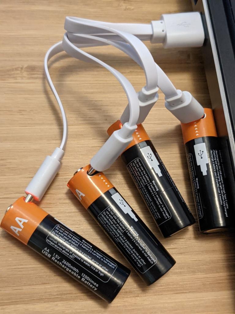 Four AA batteries with USB-C charging ports on them plugged into a laptop via a four-way splitter cable. 