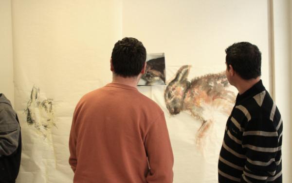 Two male-presenting humans look at a painting of a hare on a wall