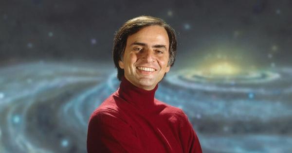 Carl Sagan in a red turtleneck standing in front of an image of a galaxy.