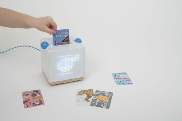 A small hand places an NFC card into a slot in a perspex box which lights up with an image relating to the music tied to the NFC
