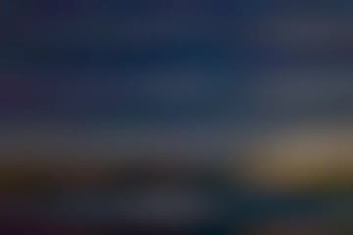 Two bright objects are pictured very near each other in night sky filled with stars. A beach is in the foreground, with some lit structures visible across the water.