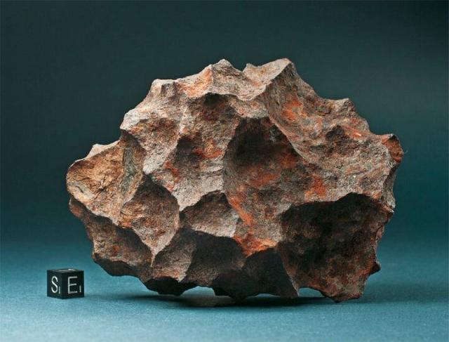 "Henbury meteorite of 1,740 g. The compact specimen exhibits sharp edges and exaggerated regmaglypts due to subsurface erosion. Scale cube at lower left of image is 1 cm on each edge (marked with white S and E)."

Meteorite Recon, CC BY-SA 3.0, via Wikimedia Commons.