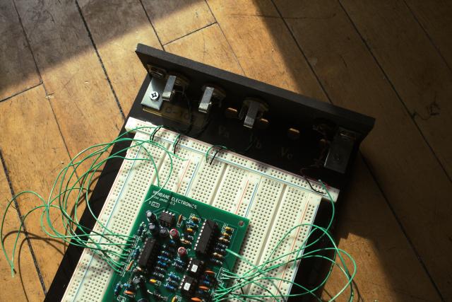 top view of an electronics test board made of an old breadboard, some wood and some jacks. On top of it is a completed pcb for a guitar pedal