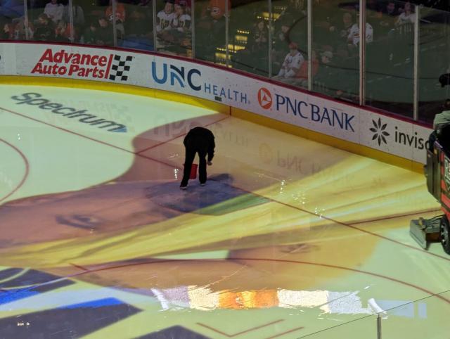 A worker doing something at a goal's post hole during intermission. 
