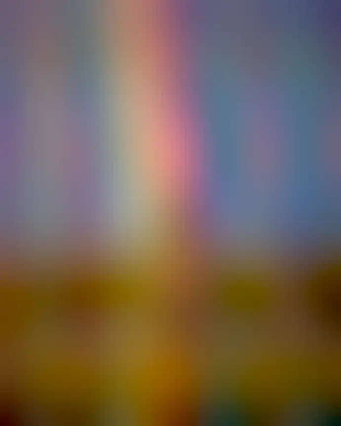 A grassy hill is seen topped by a small tree. The tree appears to be at the end of a bright and colorful rainbow.