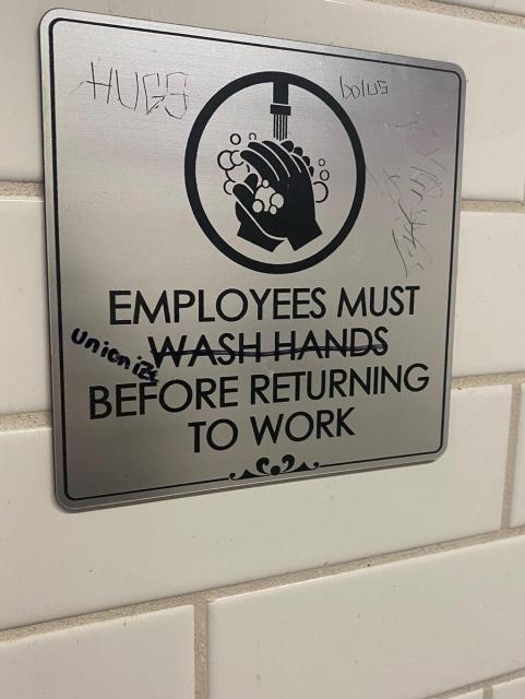 Hand washing sign on a tile wall that said "Employees must wash hands before returning to work" gut wash hands has been crossed out and replaced with unionize 