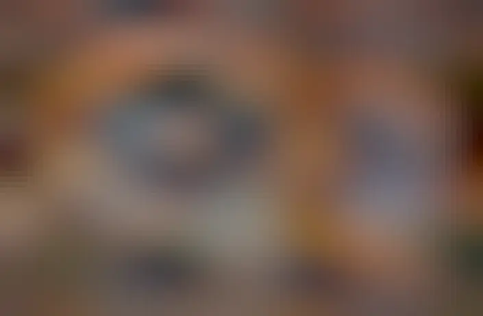 A red tinged nebula is shown in front of a starfield. Dust structures appear around the nebula's edge, and stars are also seen near the nebula's center.