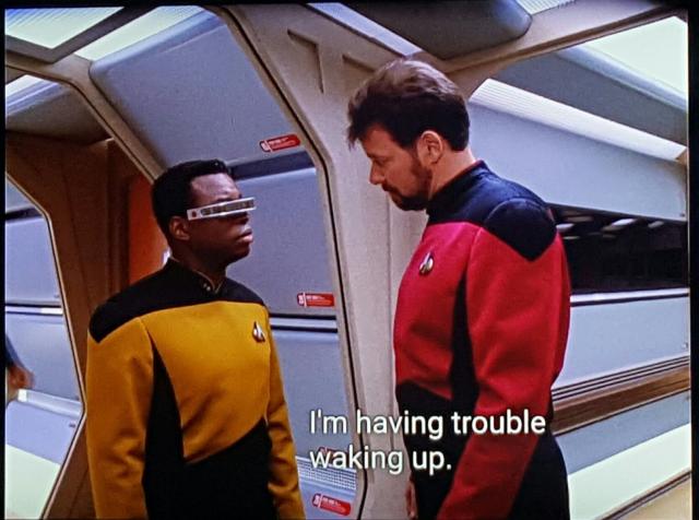 Riker and Geordi meet at a Enterprise corridor intersection. Riker is very tall. You don't always see it, but against Geordi, sheesh he's a big fella. Anyways, his hair's a bit messy. Closed caption reads, "I'm having trouble waking up."