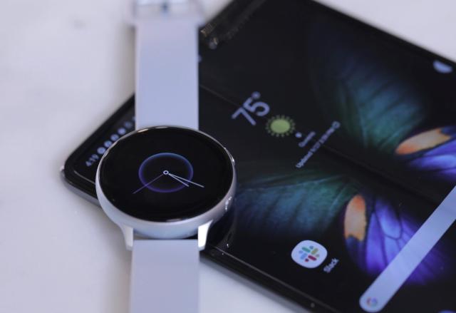 a Samsung wearable resting on top of an Android phone on a white table.