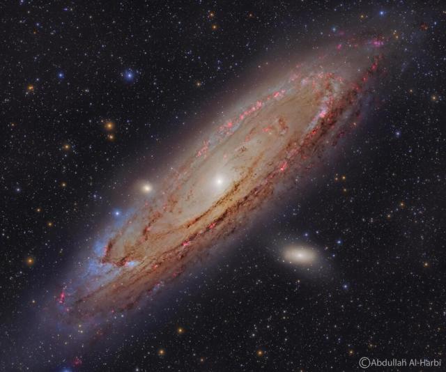 The Andromeda Galaxy is shown in great detail. Red nebulas, blue stars, and dark dust are all seen in a swirl around the galaxy's bright center.