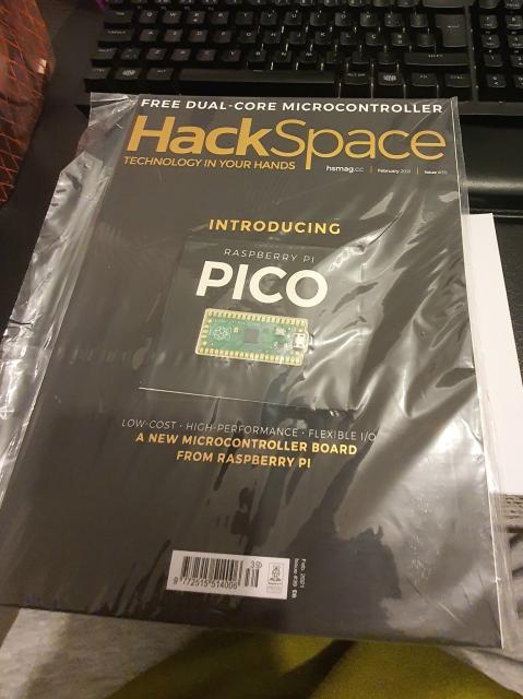 Photo of a Raspberry Pi Press' HackSpace #39 (February 2021) with the included for free Raspberry Pi Pico on the front, still closed in the plastic shrink-wrap.