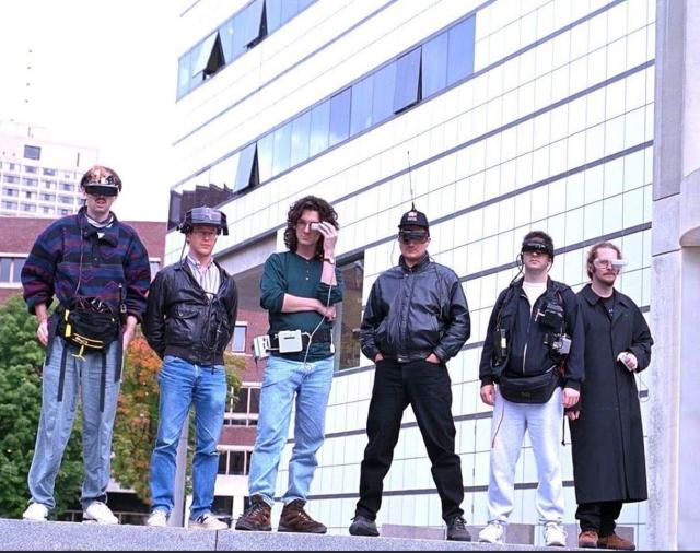 6 members of the Wearable Computing Project at MIT, wearing various 90s electronic headsets and computing equipment.