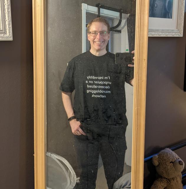 Picture in a mirror of a goofy person wearing the shirt and grinning like a dumbass.