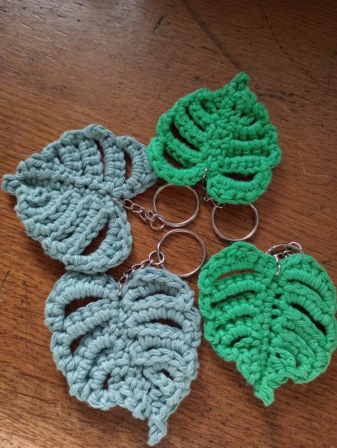 Four crocheted Monstera Keyrings. Two are in a vibrant green, the other two are in a dusty grey green.