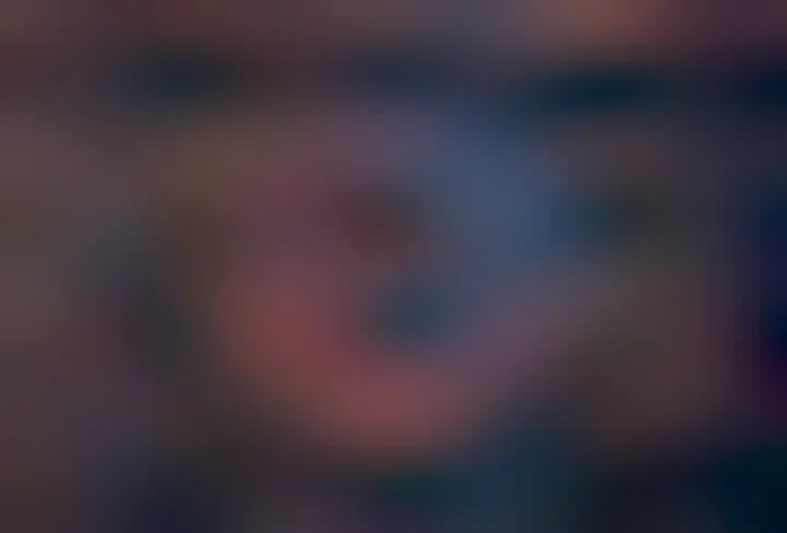 A nearly spherical but stringy nebula is shown against a starry background. The nebula is colored blue and red.