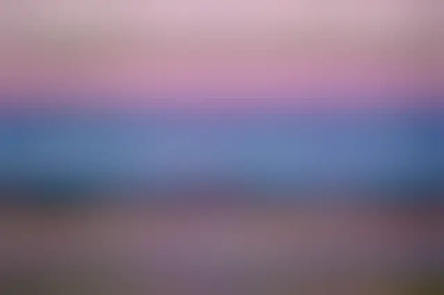 A sunset sky over Sicily is shown with, from top to bottom, a pink atmospheric band, a blue atmospheric band containing the Moon, a band with land containing buildings, and a band of water reflecting the pink and blue atmospheric bands.