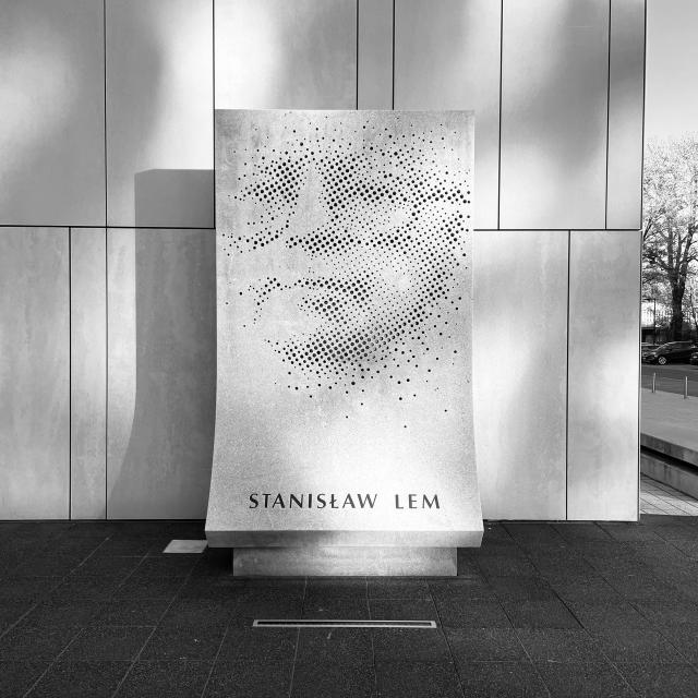A rectangular statue made out of concrete with the face of Stanisław Lem made out of drilled out halftone dots, with his name written underneath.