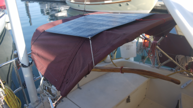 a mini and low bimini on a boat, covered with old red sunbrella canvas, with a flexible solar panel on top