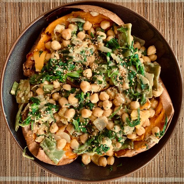Top down picture of a big plate presenting a meal. Three roasted sweet potatoes are filled with a mixture of greens and chickpeas and topped with sesame seeds.