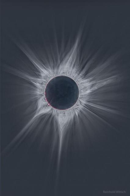 A deep image of the Sun's surrounding corona during the April 2023 total solar eclipse. The central disk is dark and many bright and complex rays are seen extending out. A few hot pink filaments can be seen just around the Sun's edge.