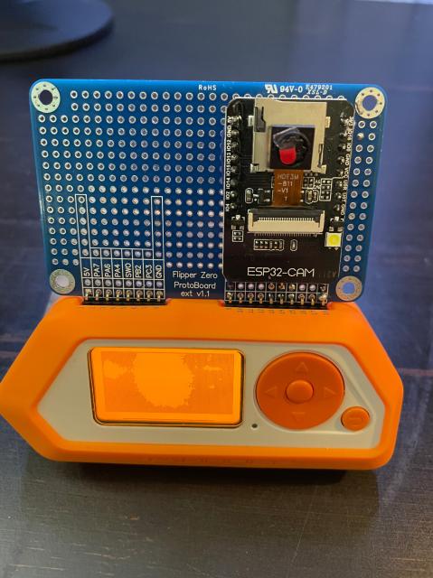 A flipper zero hacking tool with a do-it-yourself camera attached to it on a printed circuit board.