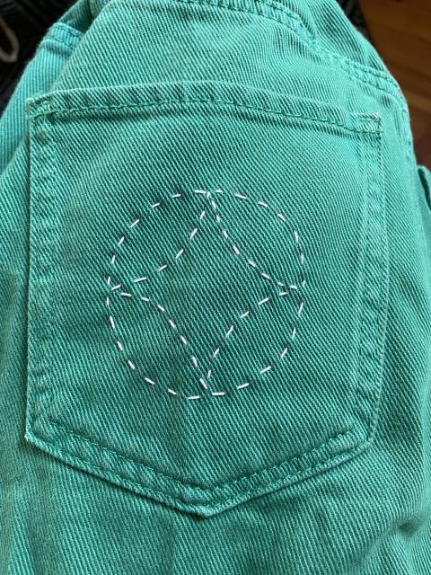 closeup of a sashiko-style sewing on a denim pant back pocket. green denim, white thread