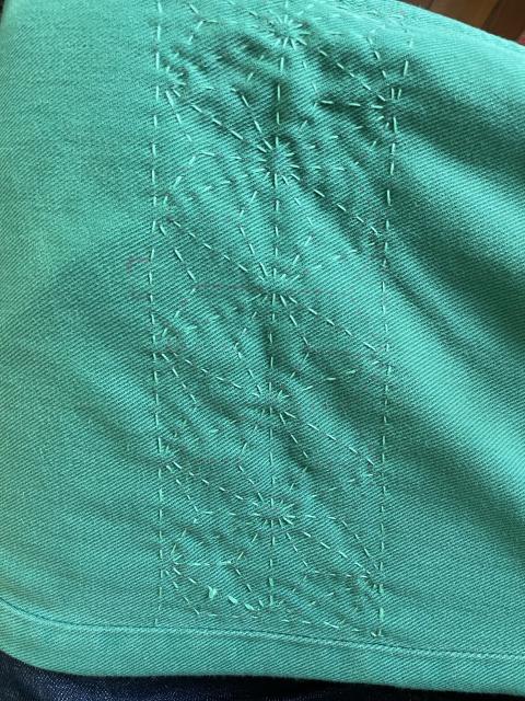 closeup of a sashiko-style sewing (almost finished) on a denim pant. 
light green thread on green denim. The sashiko pattern is “hemp leaves” I think.