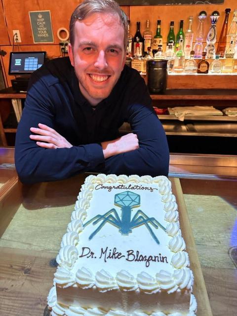 Me with a cake that reads: "Congratulations Dr. Mike Blazanin" and an image of a phage