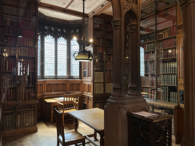 A wood paneled room with stained glass windows, every wall covered with books. John Rylands Library.