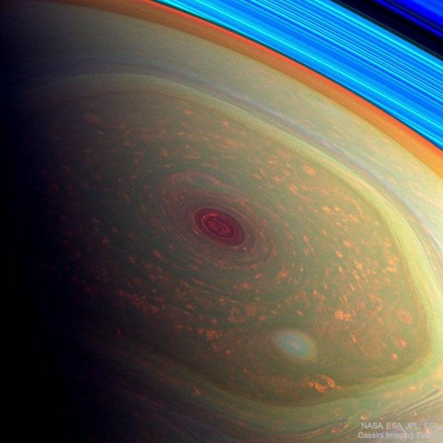 Saturn's north pole is shown with vibrant false colors. The outer boundary appears as a rounded hexagon.