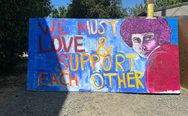 Large painted sign reading, "We must love and support each other."