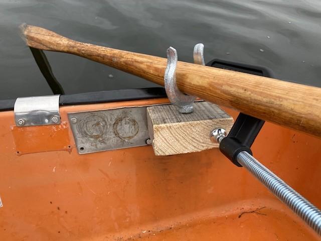 wood clamped to transom of boat. an oarlock threads the wood and an oar rests in the oarlock