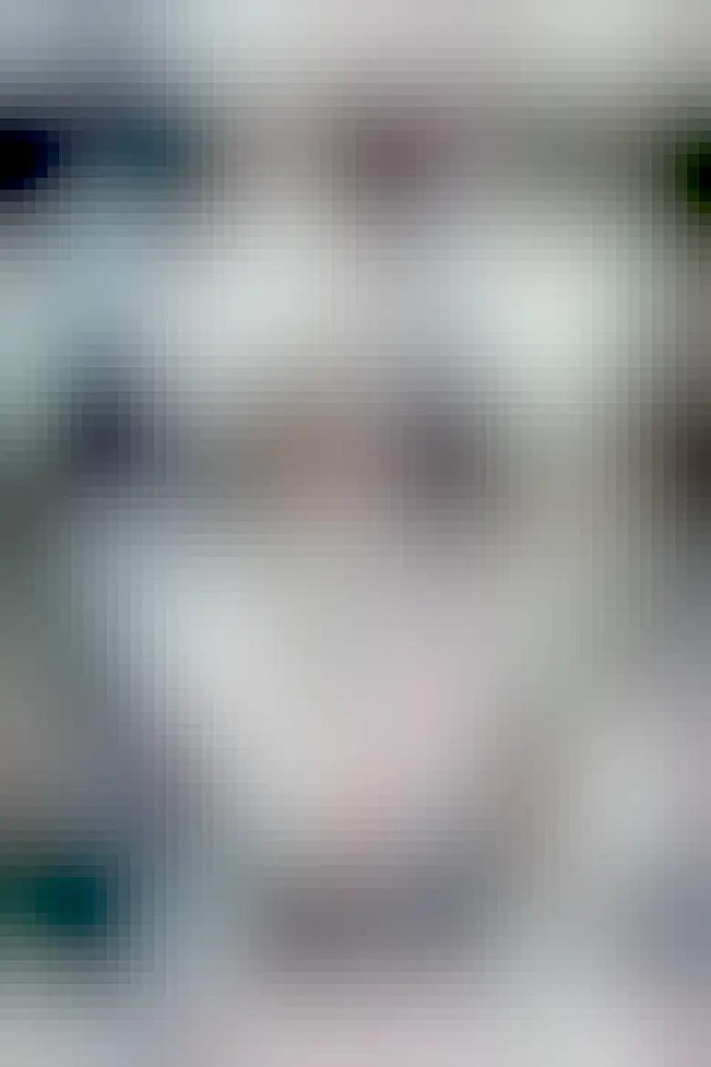 A black and white photograph of a male-identifying person using a machine to draw architectural drawings. In their left hand is a pen drawing on a screen. In their right hand they are typing on a keyboard with large buttons with unusual symbols on them.