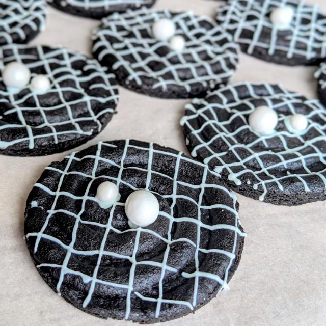 Dark cookies decorated with white icing to look like a space-time grid of merging black holes