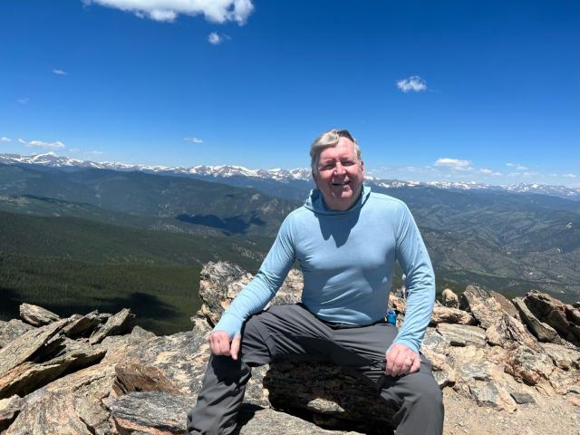Alan sitting on the top ov Chief Mountain, Colorado with more mountains in the distance.