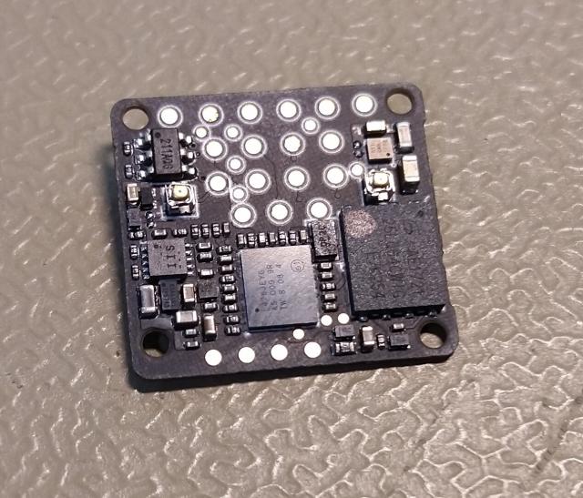Small black finger nail sized circuit board with multiple small chips.
It also features small golden testpad circles on approximately a third of it's area.