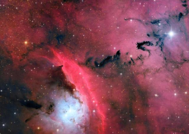 A busy star formation region is shown highlighted by red glowing clouds and dark ominously-shaped dust.