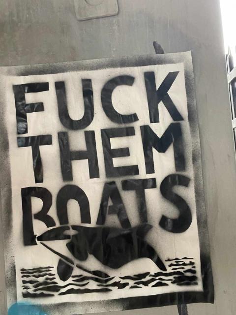 Orca stencil poster on a wall that says "Fuck them boats"