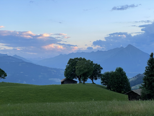 Pink sunset clouds over a mountainous landscape with lush green grass