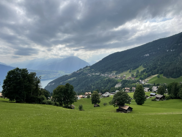 Green fields and a village on a mountain over a valley with a lake and sunbeams coming through the clouds above it