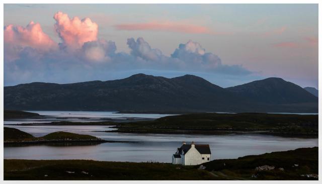 A white house on the shore at Loch Portain, North Uist as day turns to night.