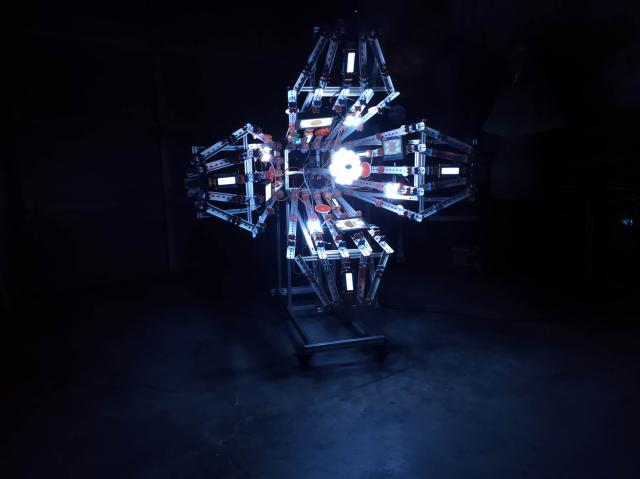 A front view of a large, trumpet-flower-shaped artwork. It glows brightly in a dark room due to the many small screens on its "petals."