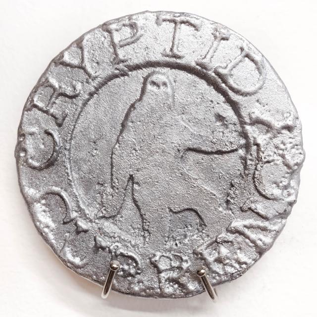 this close-up shows a well-formed token depicting Bigfoot and the words "Cryptid" and "Currency" around its edges. It is shiny and crisp.