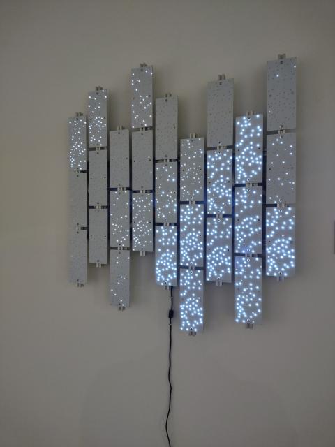 A silhouette of a person with dim rings radiating around them is shown with many small white LEDs on a patchwork of display panels. The panels are arranged in a chopped-up, glitch-like way.