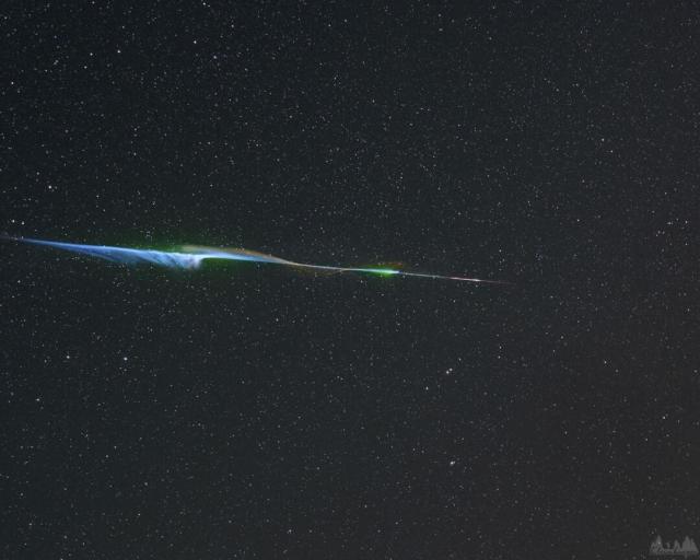 A bright colorful streak crossed the image center, which wisps of colorful gas extending out. In the background is a dark starfield.