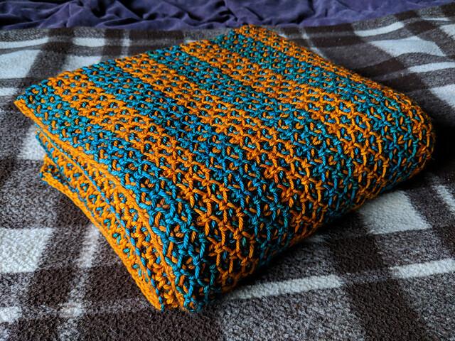 A folded blanket with wide orange and teal stripes. The knitted stitch pattern is very open.